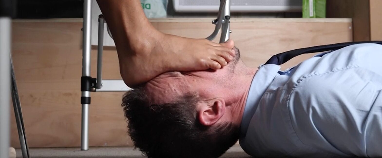 A man lying beneath a woman's bare feet during a foot worship session in London.